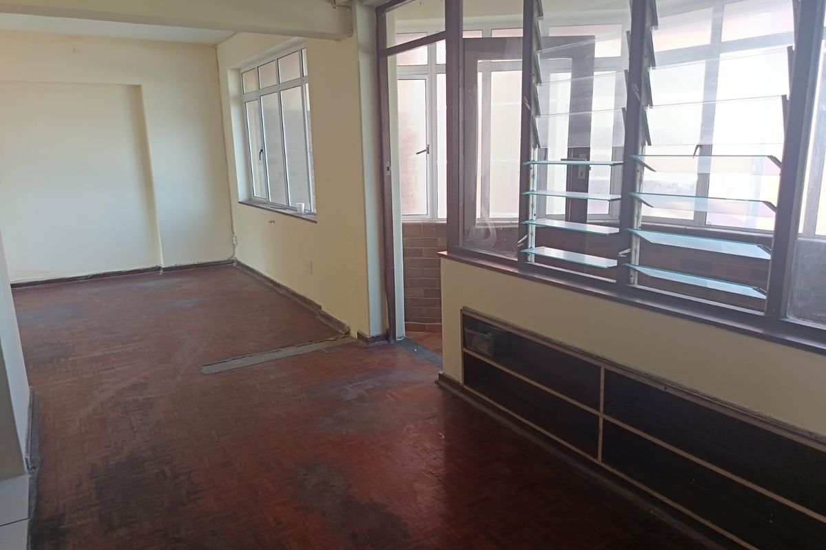 An empty living area featuring original parquet flooring, large louvre windows, and a built-in shelving unit with an internal glass partition.