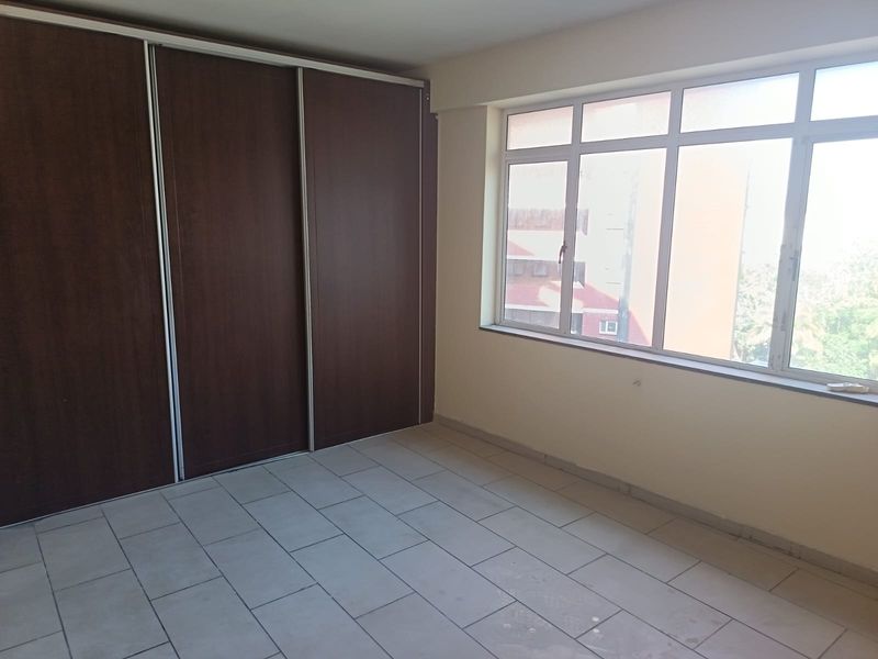 An empty bedroom featuring tiled flooring, large aluminium-framed windows, and a built-in sliding door wardrobe.