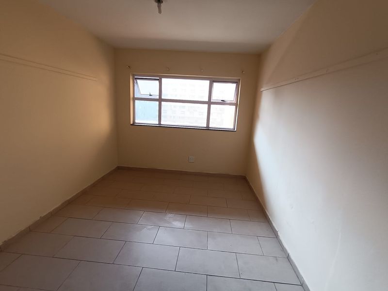 An empty bedroom featuring tiled flooring, neutral walls, and an aluminium-framed window, providing a blank canvas for potential interior design updates.