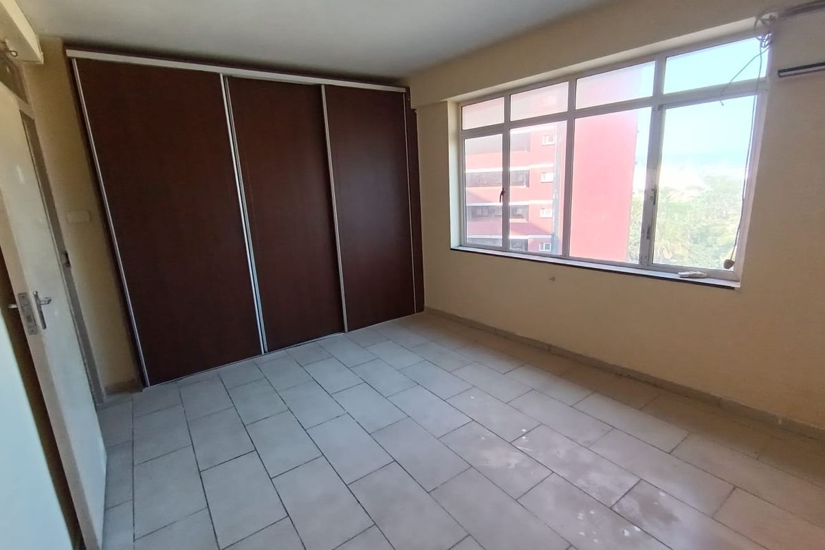 An empty bedroom featuring tiled flooring, a large window with natural light, and a built-in sliding door wardrobe.
