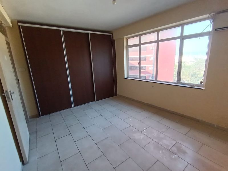 An empty bedroom featuring tiled flooring, a large window with natural light, and a built-in sliding door wardrobe.