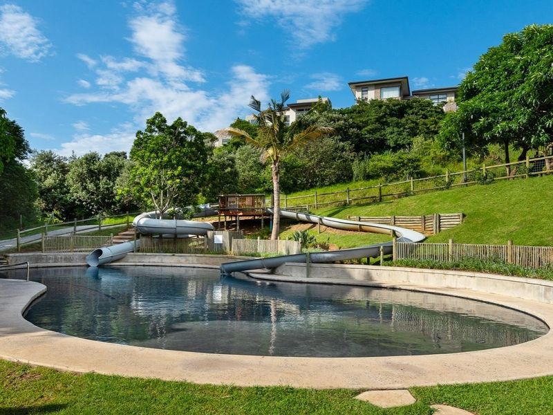 A well-maintained outdoor pool area featuring a water slide, concrete pool surround, and landscaped terraced gardens.