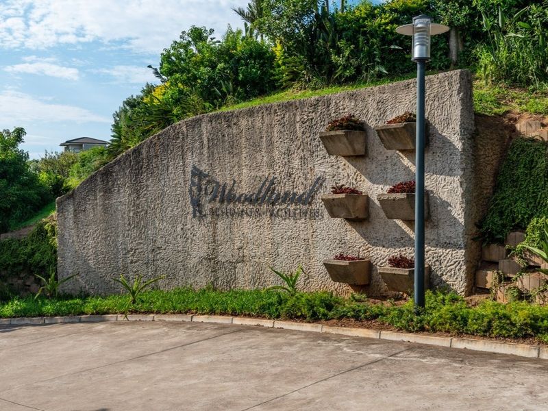 Entrance view of the residential estate featuring a textured concrete retaining wall with integrated planters and paved driveway access.