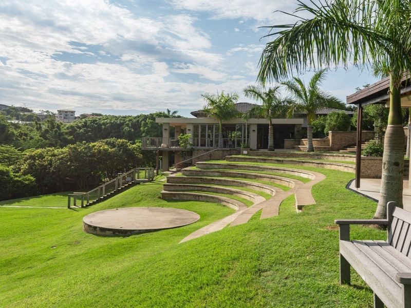 A beautifully landscaped garden featuring a unique terraced amphitheatre seating area, a central concrete stage, and lush green lawns overlooking the property.