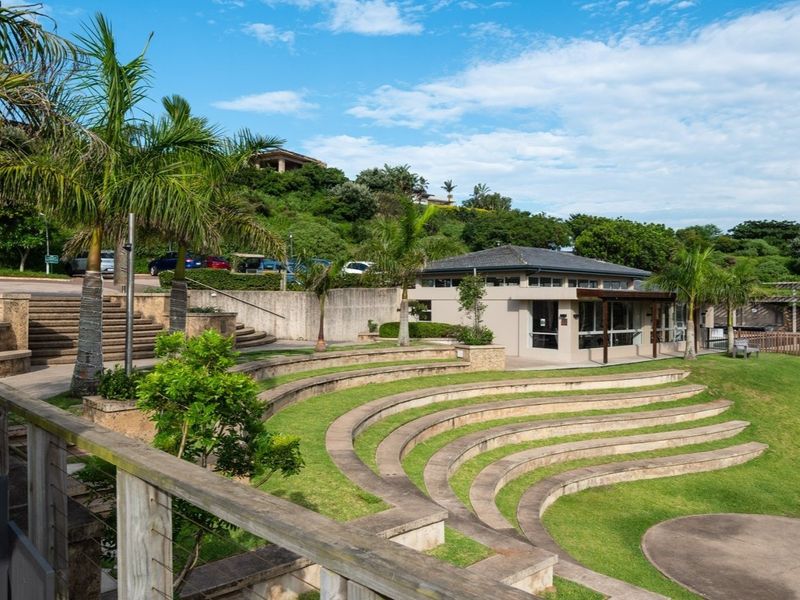 A well-maintained outdoor amphitheatre and clubhouse facility featuring tiered concrete seating, manicured lawns, and landscaped surroundings within a residential estate.