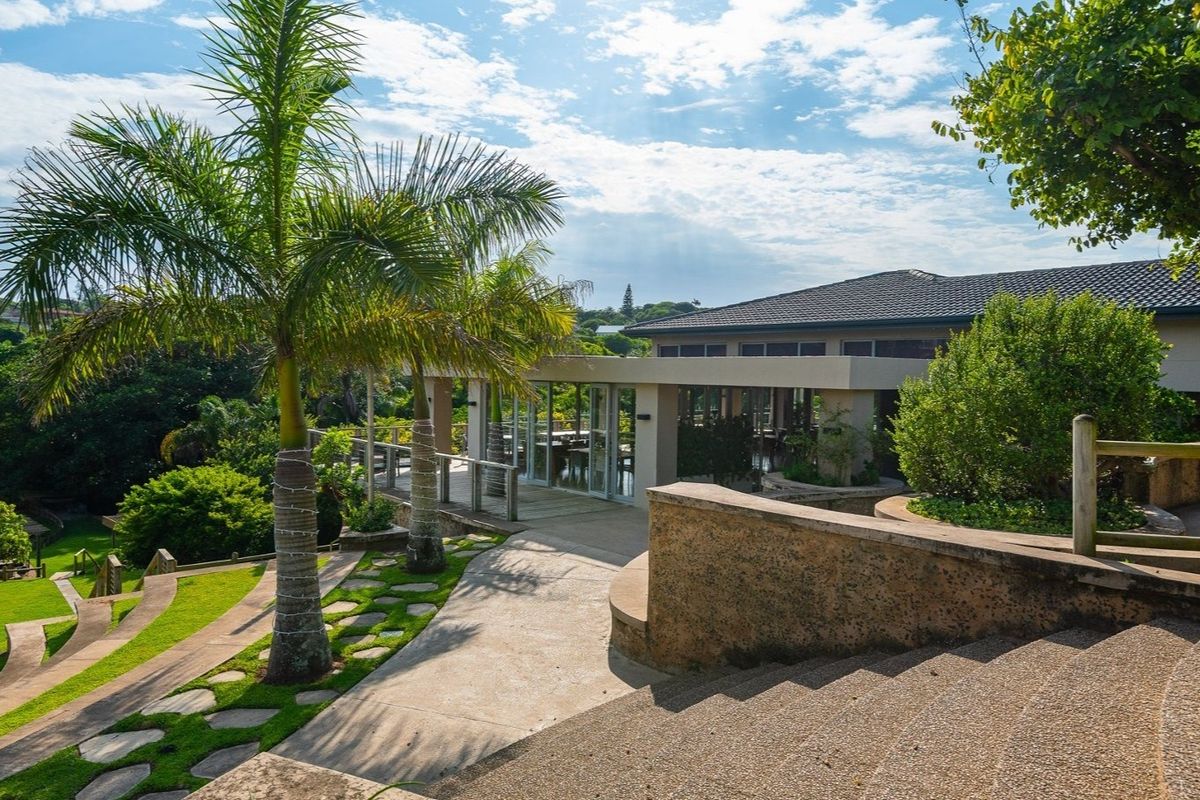 A well-maintained rear exterior view featuring a concrete pathway, landscaped garden, timber decking, and access to the main dwelling through glass sliding doors.