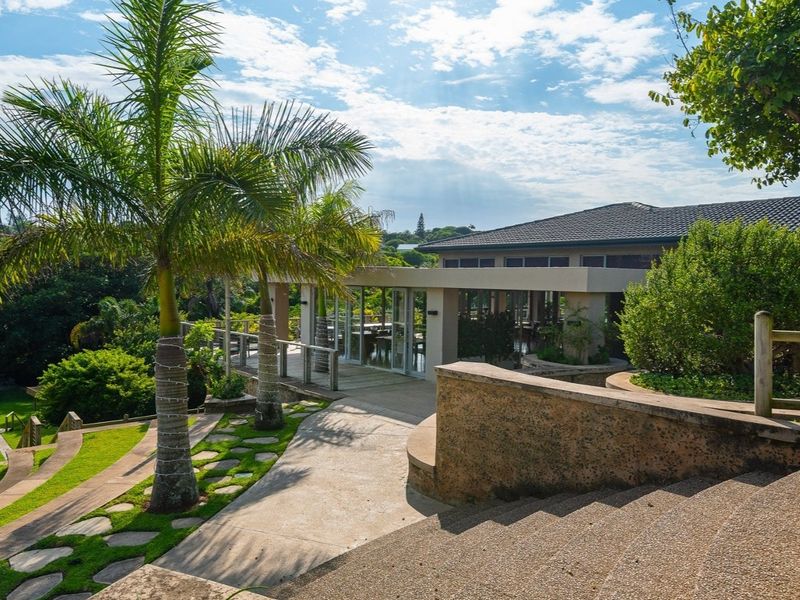 A well-maintained rear exterior view featuring a concrete pathway, landscaped garden, timber decking, and access to the main dwelling through glass sliding doors.