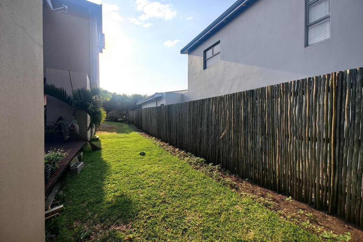 A side garden area featuring a natural wooden pole fence, a small timber deck section, and a grass lawn between two residential structures.
