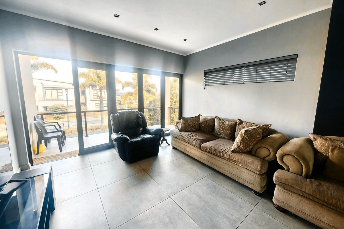 A bright living room featuring large sliding glass doors leading to a balcony, neutral tiled flooring, and recessed ceiling lighting.