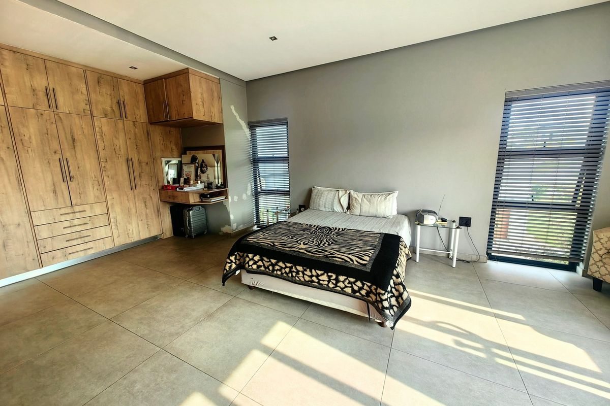 Spacious bedroom featuring large-format floor tiles, extensive built-in wooden cabinetry, and dual windows with venetian blinds.