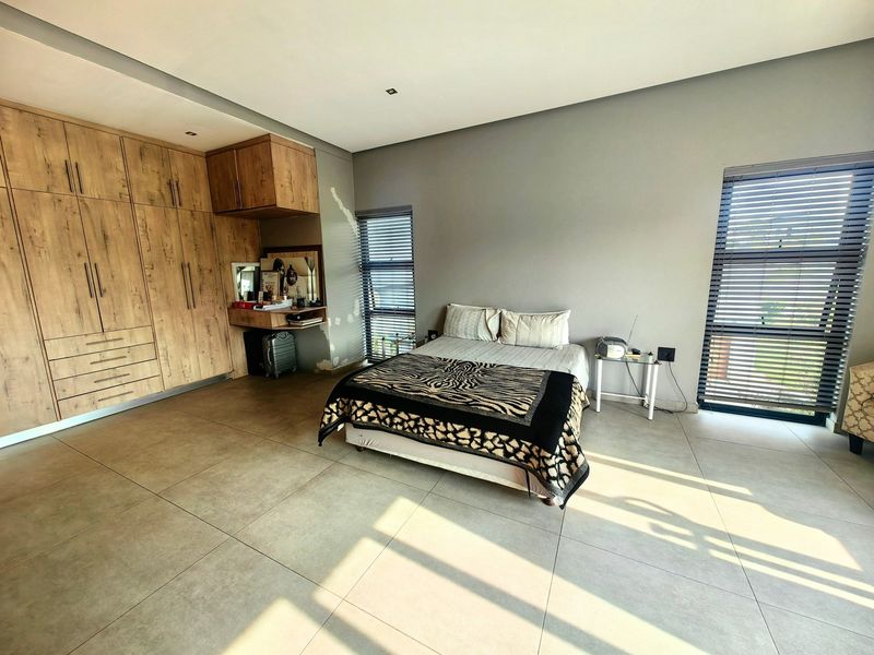 Spacious bedroom featuring large-format floor tiles, extensive built-in wooden cabinetry, and dual windows with venetian blinds.