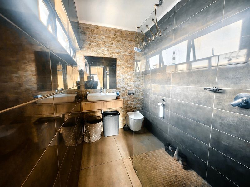 Modern bathroom featuring a wall-mounted vanity with vessel sink, wall-hung toilet, stone feature wall, and a spacious walk-in shower with glass screen.