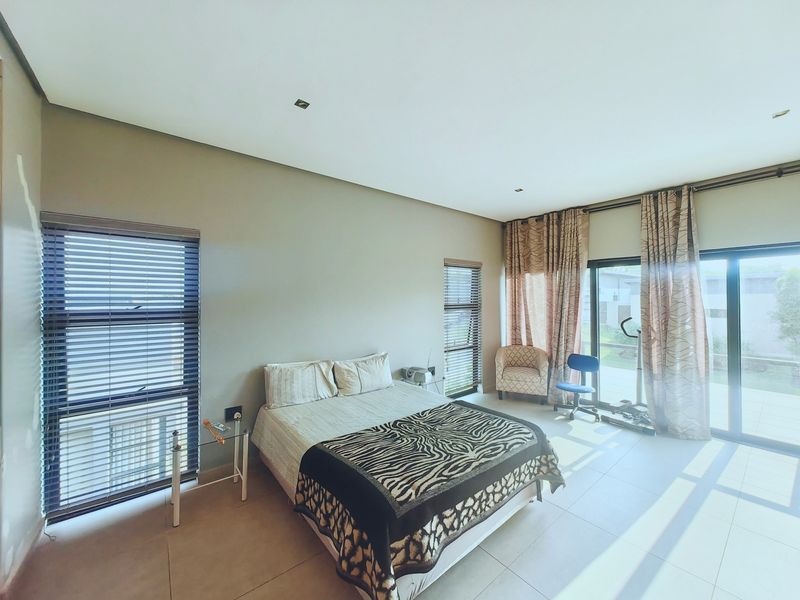 Spacious bedroom featuring neutral tiled flooring, recessed lighting, and large sliding glass doors providing access to the outdoor area.