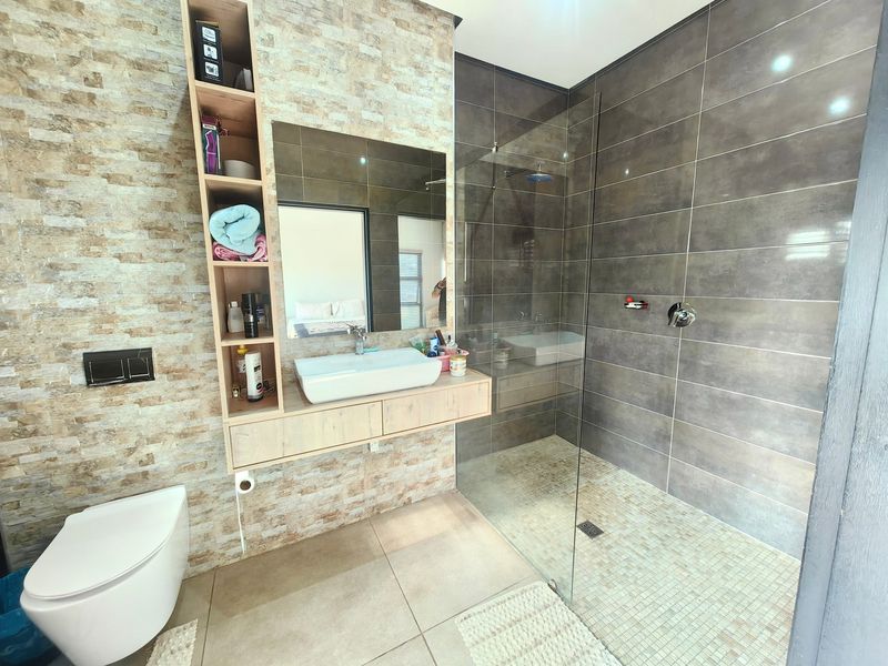 Modern bathroom featuring a floating vanity with vessel sink, built-in shelving, wall-mounted toilet, and a spacious walk-in shower with glass enclosure.