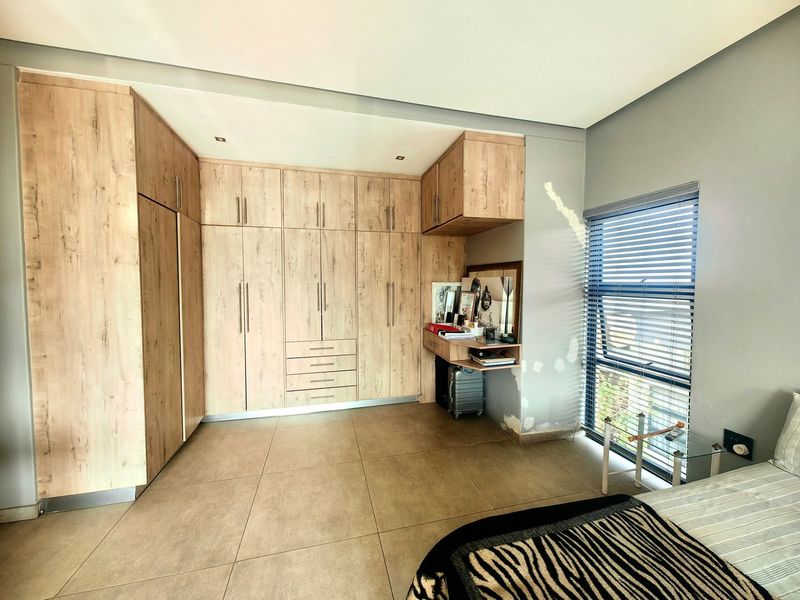 Bedroom featuring extensive built-in wooden cabinetry, tiled flooring, and large windows with venetian blinds, offering ample storage space.
