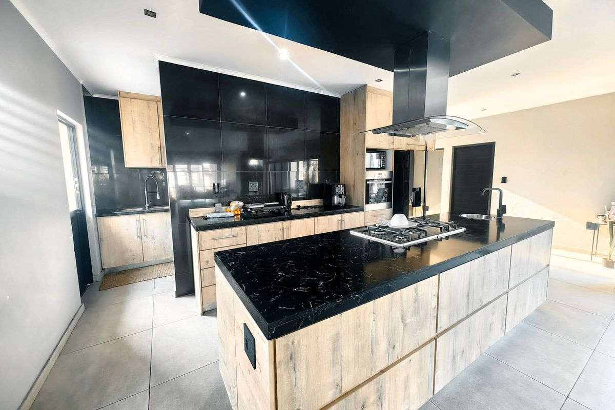Modern kitchen featuring a large island with gas hob, sleek black cabinetry, stone countertops, and integrated appliances in a contemporary open-plan layout.