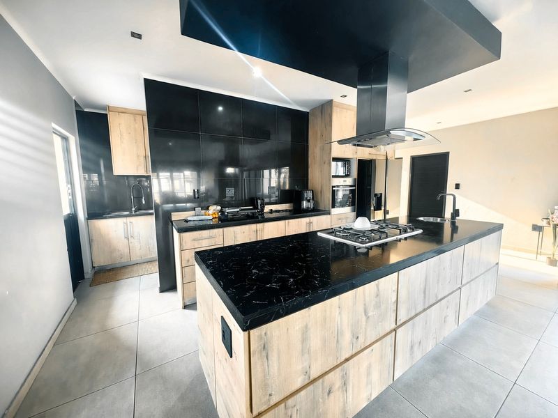 Modern kitchen featuring a large island with gas hob, sleek black cabinetry, stone countertops, and integrated appliances in a contemporary open-plan layout.