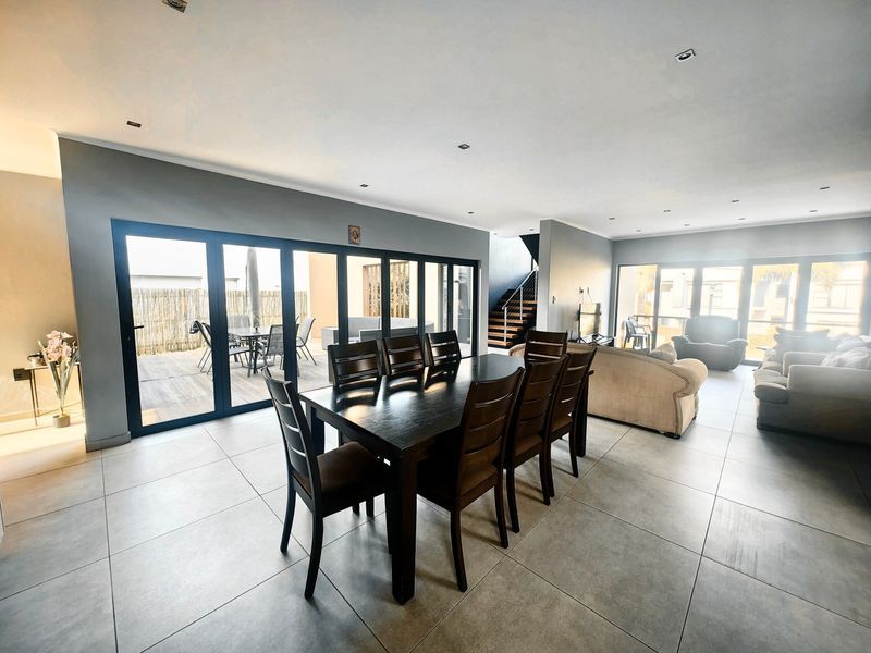 Spacious open-plan living and dining area featuring large format floor tiles, recessed lighting, and expansive black aluminium stacking doors leading to the patio.