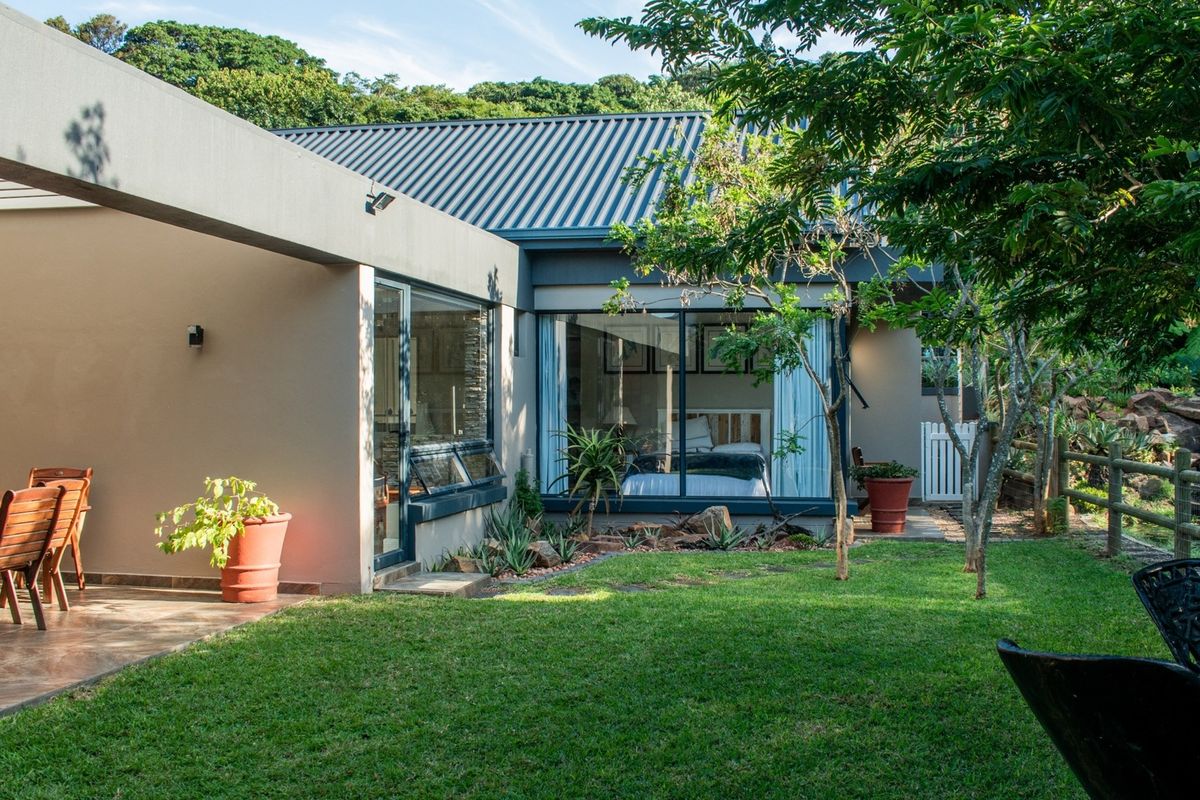 A well-maintained rear exterior view featuring a covered patio, landscaped garden, and large glass doors providing seamless indoor-outdoor flow.