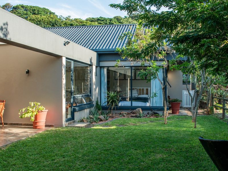 A well-maintained rear exterior view featuring a covered patio, landscaped garden, and large glass doors providing seamless indoor-outdoor flow.
