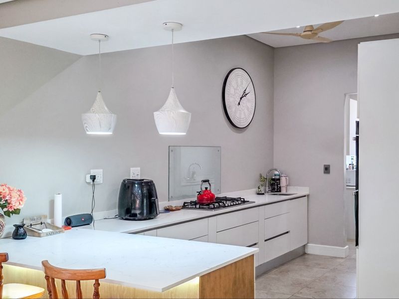 Modern kitchen featuring sleek handleless cabinetry, stone countertops, a gas hob, and stylish pendant lighting, creating a functional and contemporary culinary space.