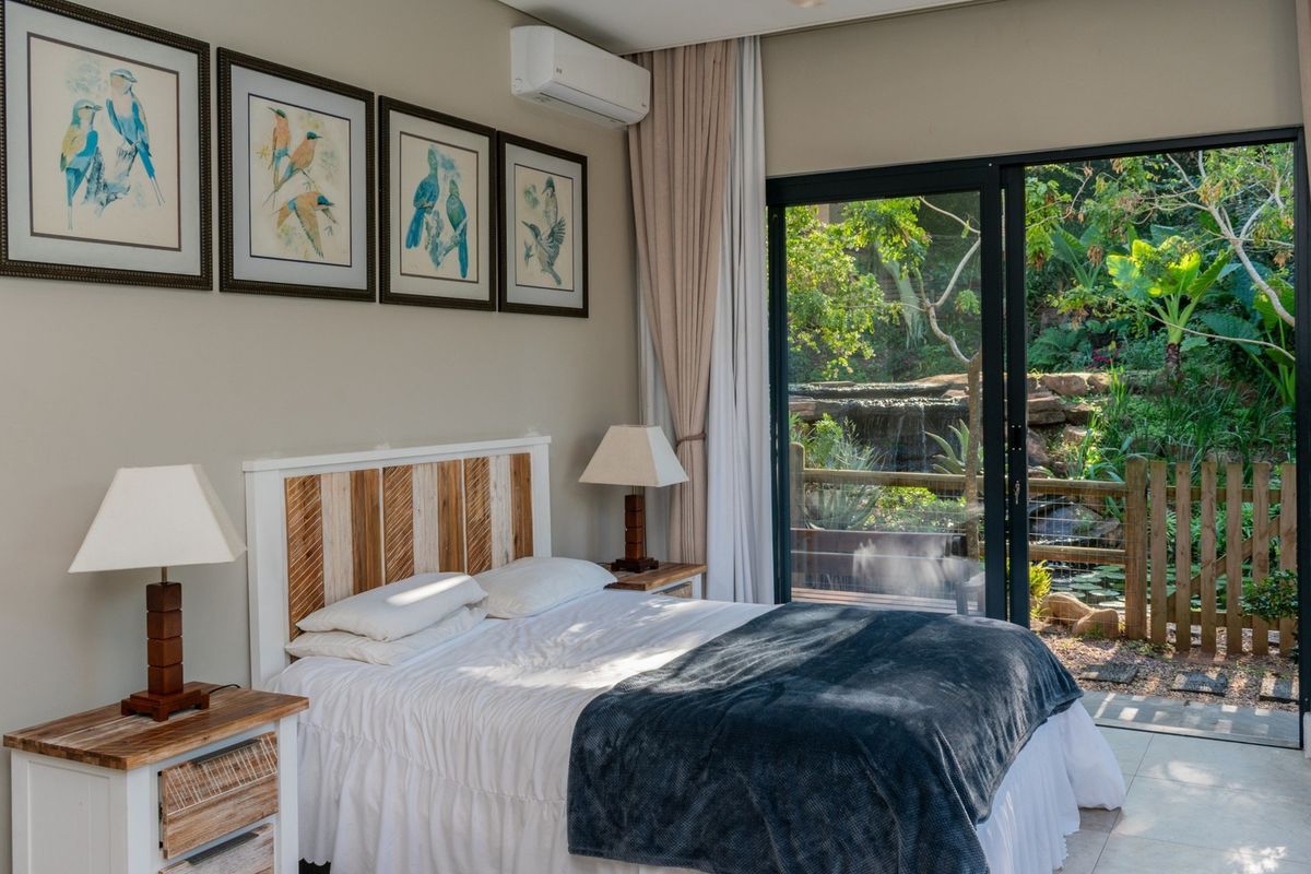 A well-maintained bedroom featuring tiled flooring, a split-system air conditioner, and large sliding glass doors that open to a lush garden view.