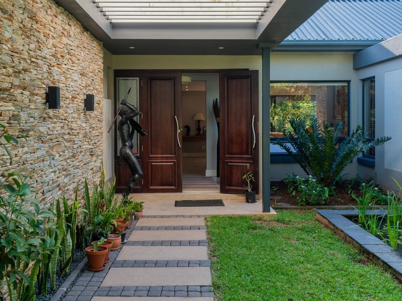Inviting entrance featuring a stone-clad wall, modern pergola, double timber doors, and a tranquil water feature set within a landscaped garden.