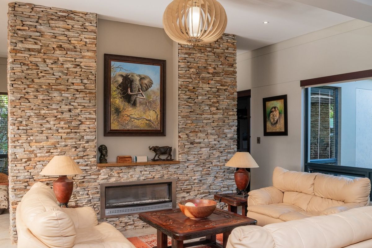 Spacious living room featuring a prominent stone-clad feature wall with a built-in fireplace, recessed lighting, and large windows providing natural light.