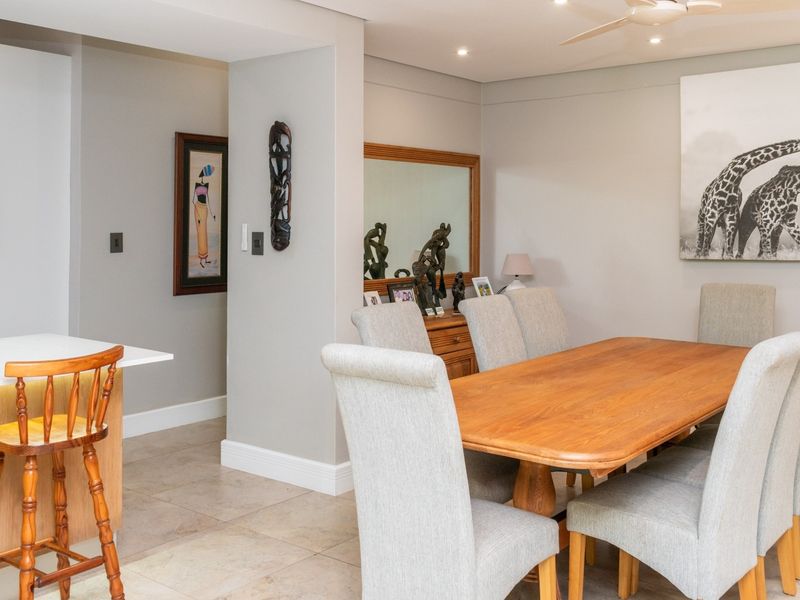 An open-plan dining and kitchen area featuring tiled flooring, a modern kitchen island with built-in oven, and recessed ceiling lighting.