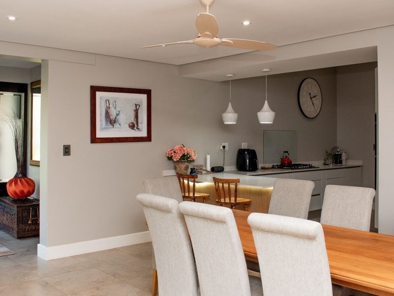 An open-plan living and dining area featuring a modern kitchen island, recessed and pendant lighting, and neutral tiled flooring throughout.