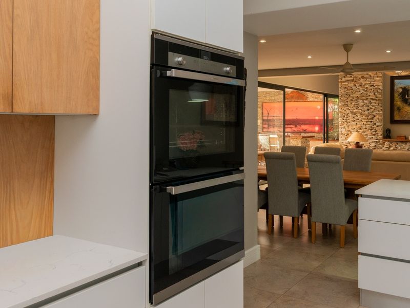 Modern open-plan kitchen and living area featuring a built-in double oven, stone feature wall, and seamless flow to the outdoor patio.