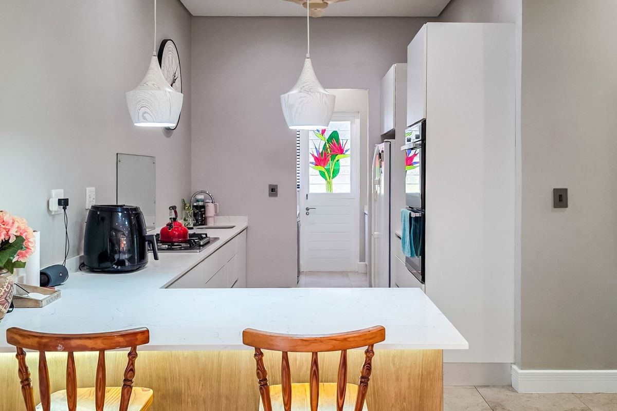 Modern kitchen featuring white cabinetry, quartz countertops, built-in oven, gas hob, and stylish pendant lighting with an integrated breakfast bar.