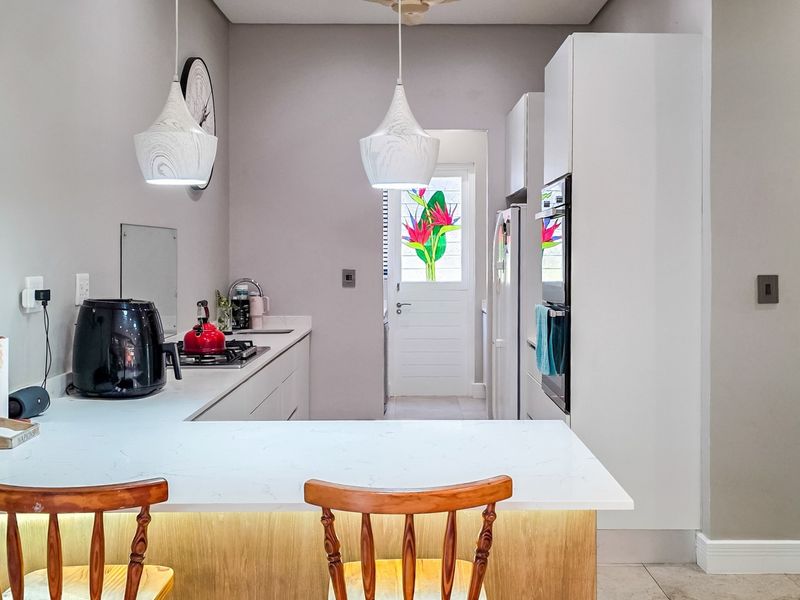 Modern kitchen featuring white cabinetry, quartz countertops, built-in oven, gas hob, and stylish pendant lighting with an integrated breakfast bar.