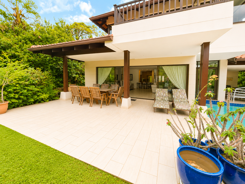 Spacious covered patio area featuring tiled flooring, direct access to the swimming pool, and seamless indoor-outdoor flow through large sliding glass doors.