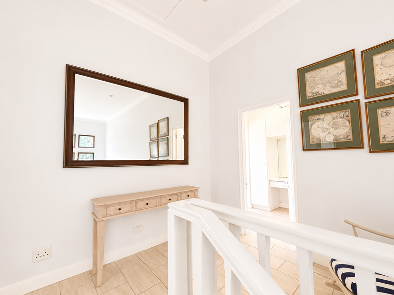 A bright and well-maintained hallway featuring tiled flooring, crown molding, and a white staircase balustrade, leading towards an adjacent room.