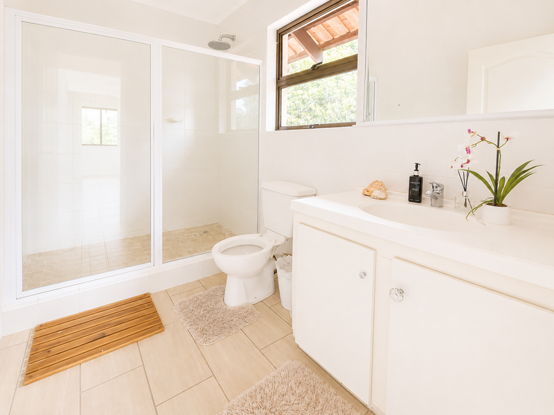 A clean and functional bathroom featuring a glass-enclosed shower, a white vanity with basin, and neutral tiled flooring.