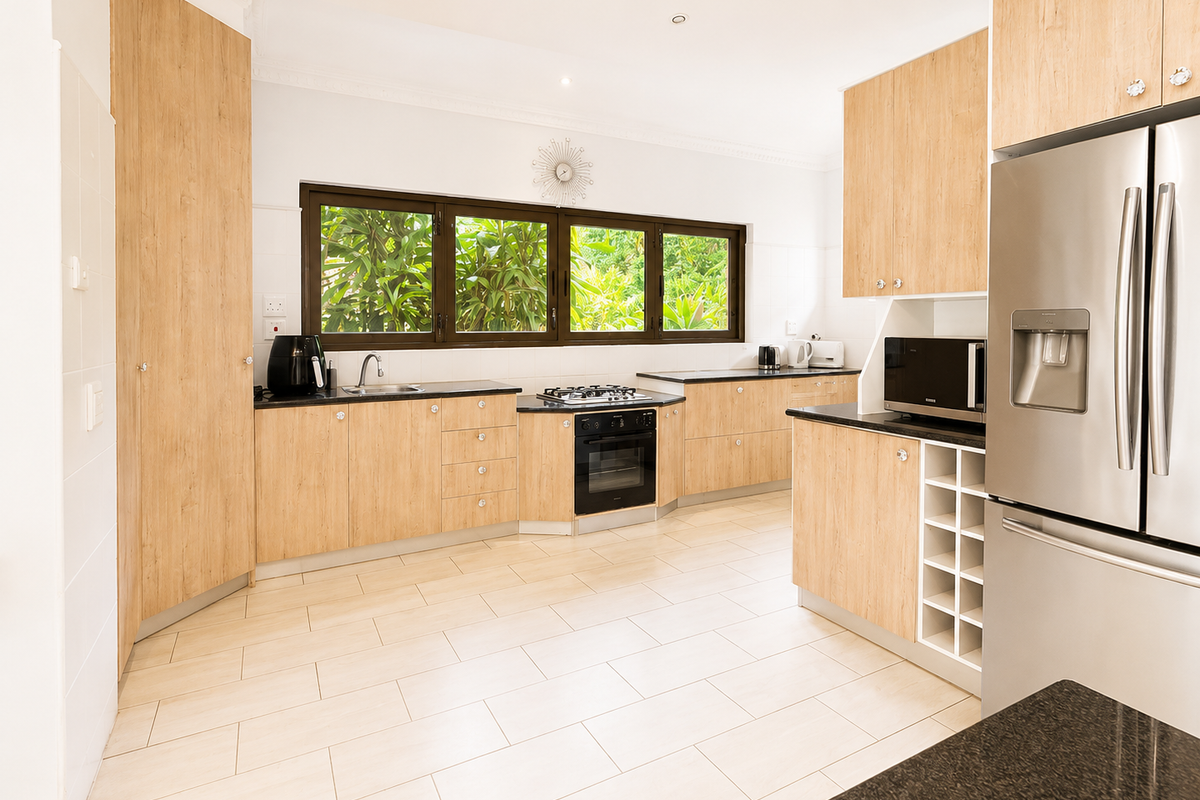 Modern kitchen featuring light wood-finish cabinetry, dark stone countertops, integrated appliances, and a functional layout with ample storage and natural light.