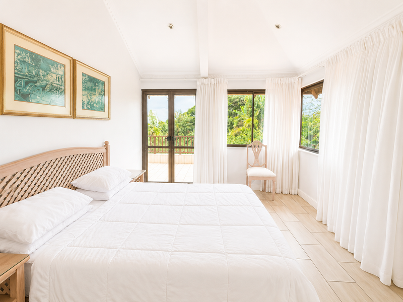 Bright and airy bedroom featuring vaulted ceilings, tiled flooring, and direct access to an outdoor balcony through sliding glass doors.