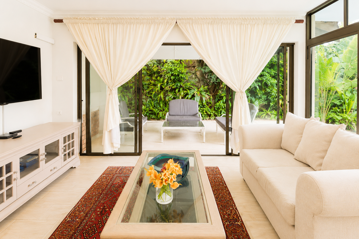 Bright living room featuring large sliding glass doors that open onto a lush garden patio, complemented by neutral tiled flooring and recessed lighting.