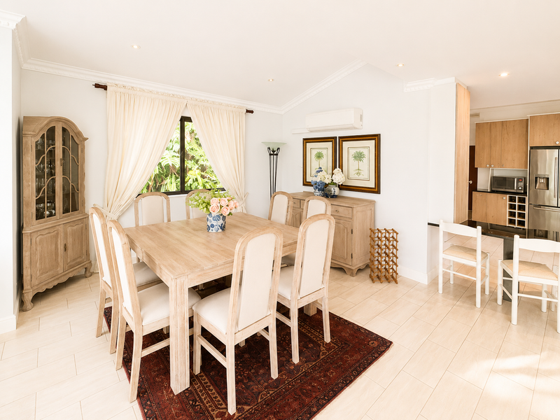 Bright open-plan dining area featuring tiled floors, crown molding, and a seamless transition into a modern kitchen with built-in cabinetry and appliances.