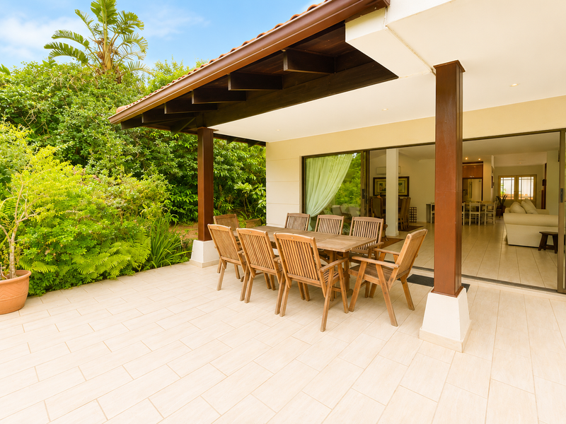 A covered outdoor patio featuring tiled flooring, timber support columns, and exposed rafters, providing seamless access to the interior living space through sliding glass doors.