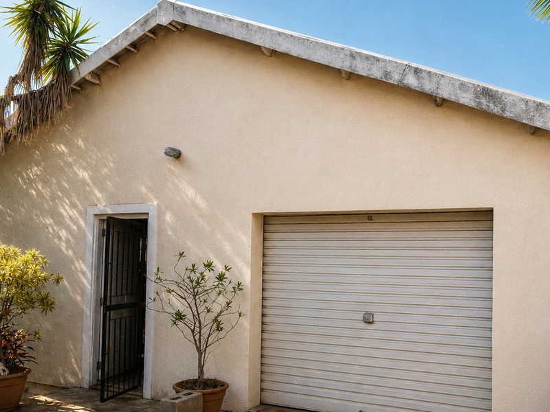 A detached garage featuring a roller shutter door and a side security entrance, with a gable roof design.