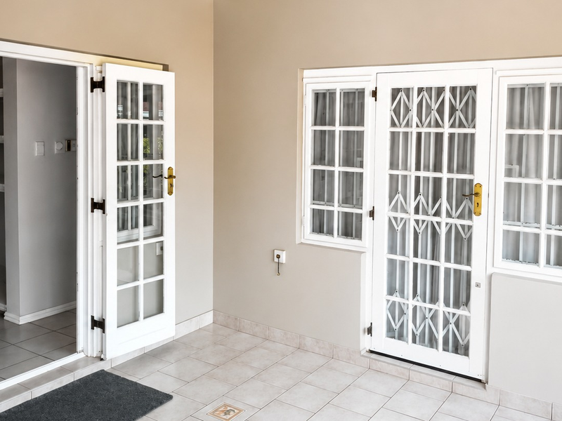 A clean, tiled patio area featuring white security gates, french doors, and access to an interior storage space with built-in shelving.