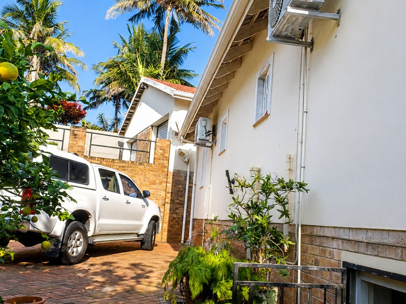 Side exterior view of the property featuring brick paving, brick walling, and mounted air conditioning units under exposed rafters.