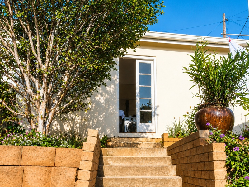 Rear exterior view of the property featuring a concrete staircase leading to a french door entrance, complemented by a retaining wall and garden.
