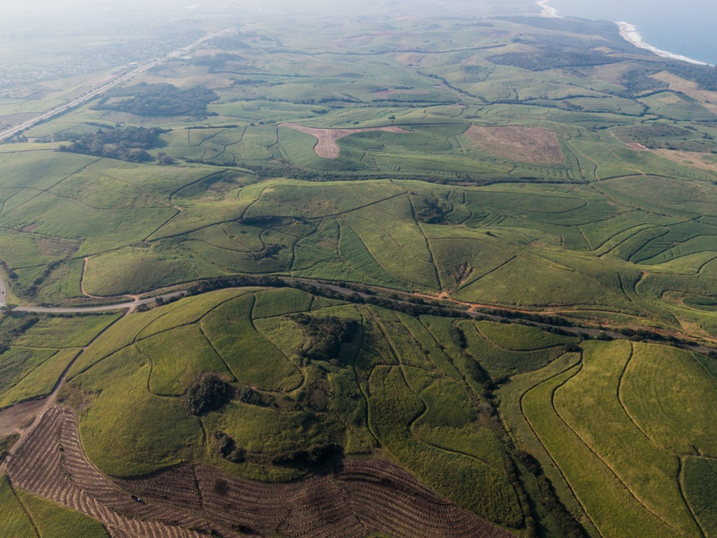 An expansive aerial view of the farm property, showcasing vast agricultural fields, proximity to the highway, and coastal landscape.