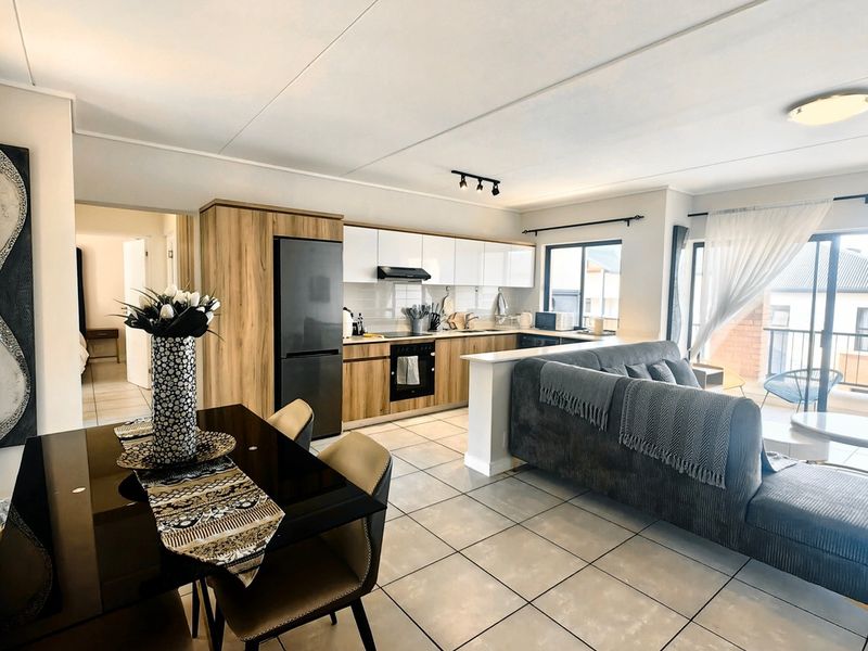 Modern open-plan living area featuring a contemporary kitchen with wood-finish cabinetry, tiled floors, and seamless access to an outdoor balcony through sliding glass doors.