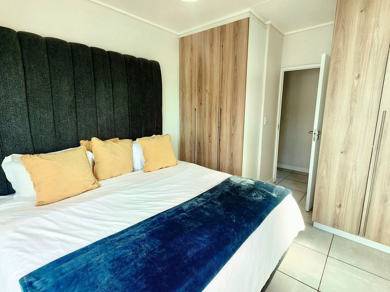 A well-maintained bedroom featuring light wood-finish built-in cupboards, modern tiled flooring, and a central ceiling fan.