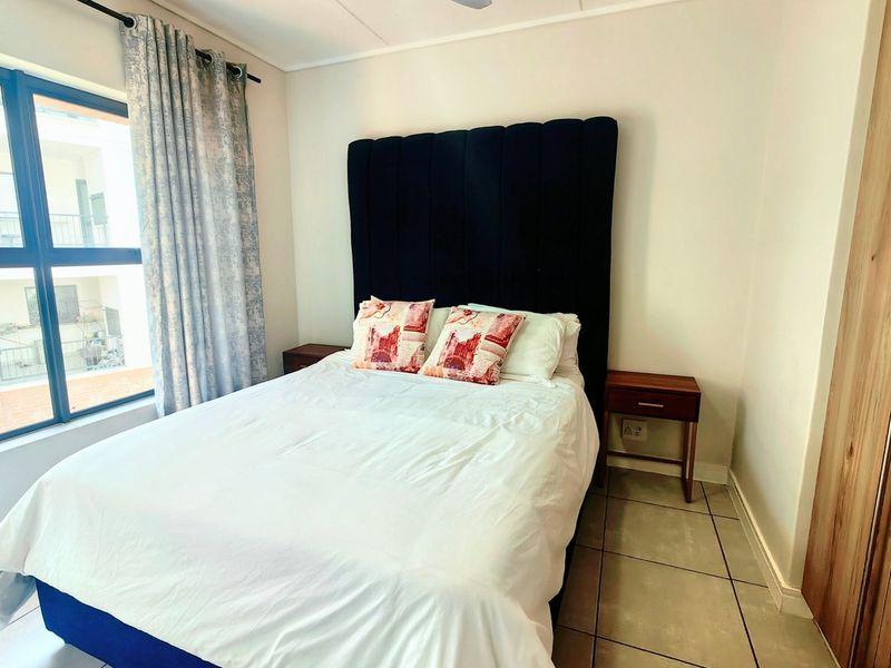A well-lit bedroom featuring tiled flooring, a ceiling fan, and a built-in cupboard, offering a comfortable and functional living space.