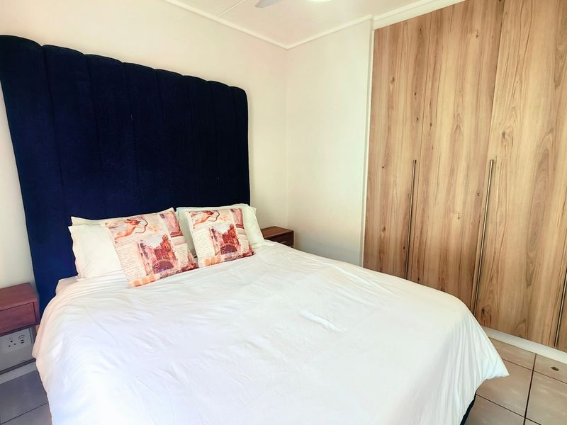 A well-maintained bedroom featuring modern wood-finish built-in cupboards, tiled flooring, and a central ceiling fan.